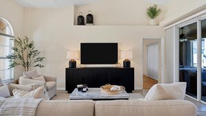 A modern living room with a large flat-screen TV, dark wood cabinet, and a beige sofa. - Punta Gorda Isles 3 Bedroom Pool+Hot Tub Home (Punta Gorda)