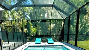 A swimming pool with clear blue water, surrounded by a covered area with two lounge chairs. - New-North Port Florida -Heated pool - 5 BED (North Port)