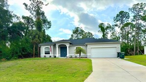 A single-story house with a front garage, a well-maintained lawn, and a clear sky. - New-North Port Florida -Heated pool - 5 BED (North Port)