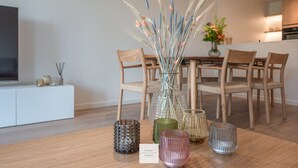 A dining area with a wooden table, chairs, a vase with dried plants, and decorative glassware.
