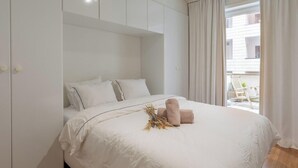 A bedroom with a large bed, white bedding, and a view of the outside balcony.
