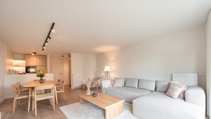 A modern living room with a grey sofa, a wooden coffee table, and a dining area with a wooden table and chairs.