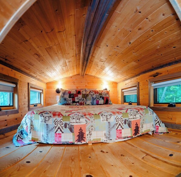 Une chambre confortable, aménagée dans un chalet en bois, avec un grand lit, deux fenêtres et un plafond en pente.