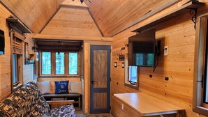 L’intérieur chaleureux d’un chalet, avec un revêtement mural en bois, un canapé agrémenté de coussins à motifs, un banc, une petite table et un téléviseur fixé au mur.