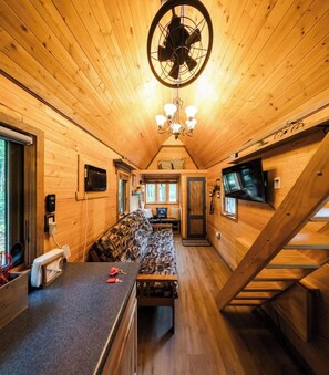 Ein Ferienhaus-Innenraum mit Holzboden, einer Couch, einem Esstisch, einem Fernseher und einem Ventilator.