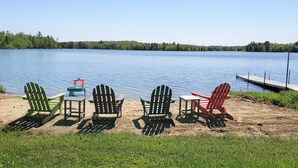 Un cadre idyllique au bord du lac, avec plusieurs chaises Adirondack et une petite table, un quai et un bateau.