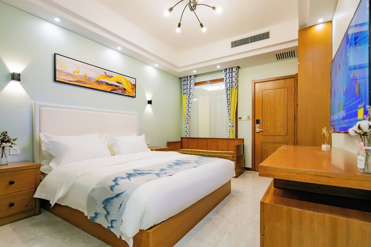 Ein Hotelzimmer mit einem großen Bett, einem Holzkopfteil, Nachttischen, einem Schreibtisch und einem Fernseher.