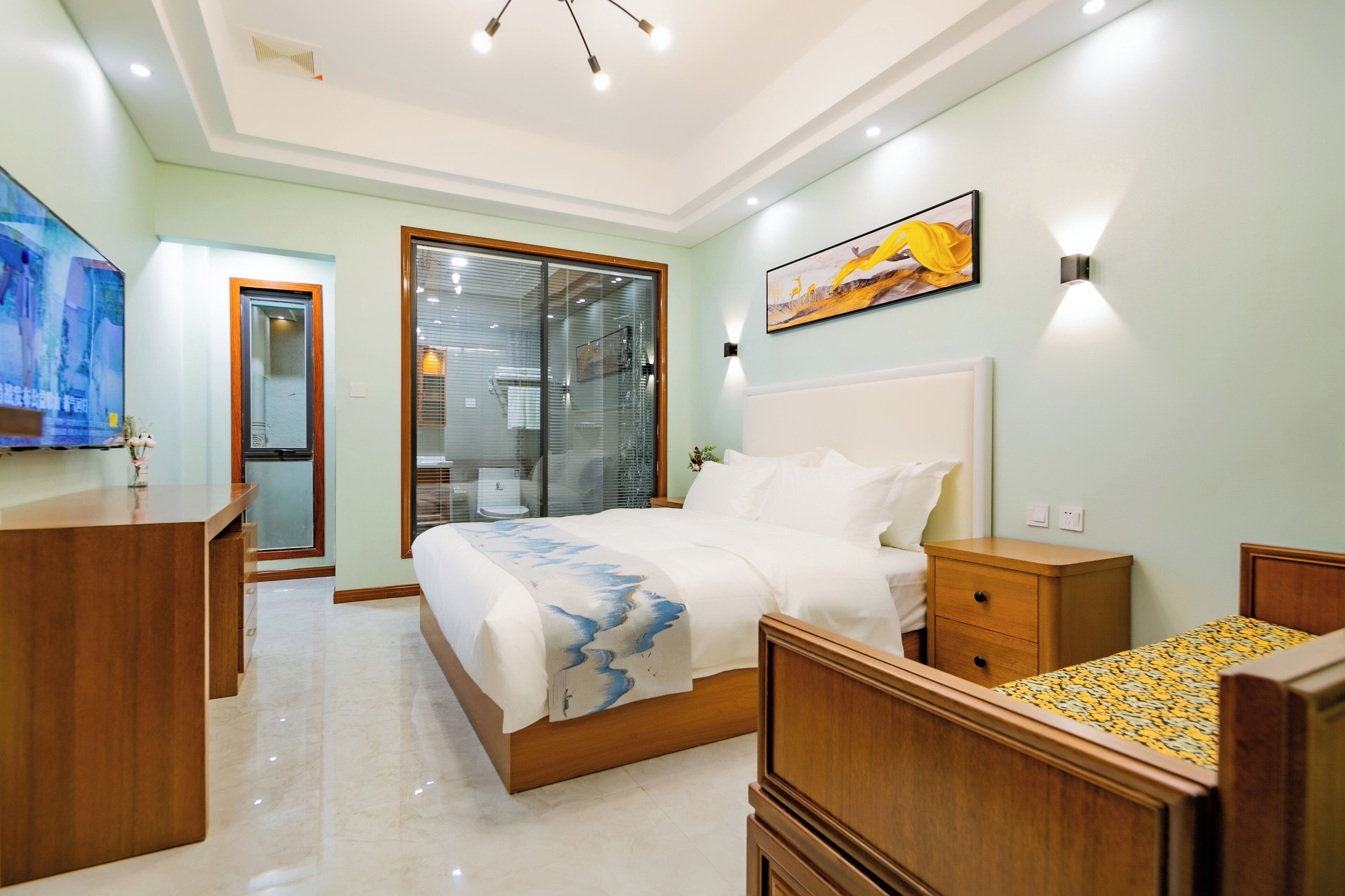 A bedroom with a bed, bedside tables, a desk, and a large window.