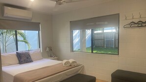 Ein Hotelzimmer mit Bett, einer Sitzbank, einem Fenster mit Blick auf einen Innenhof und einer Klimaanlage.