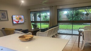 Eine moderne Küche mit einer großen Kochinsel, ein Essbereich mit Korbstühlen und große Fenster mit Blick auf den Garten.