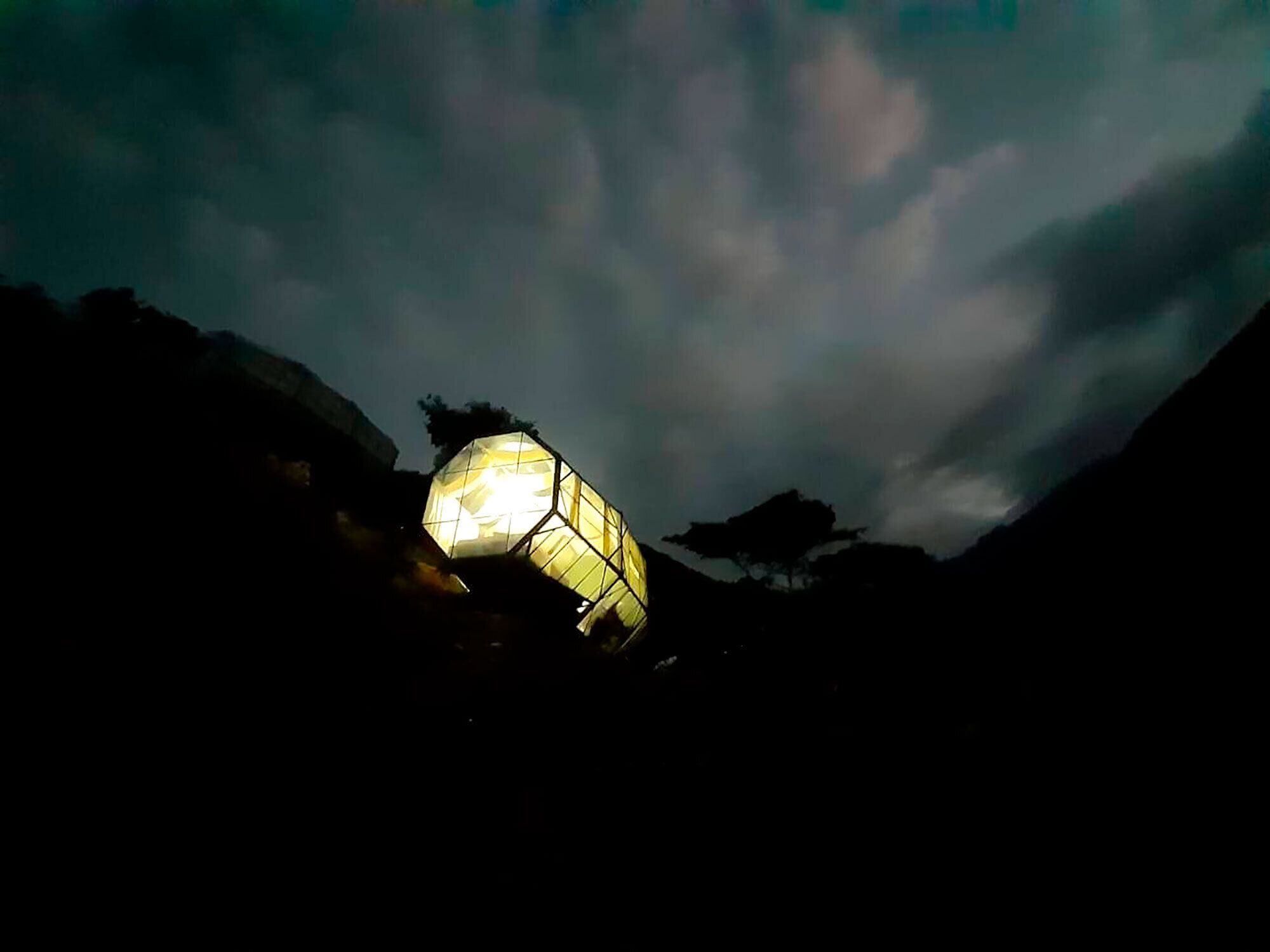 A hexagonal lantern structure illuminated against a cloudy sky.
