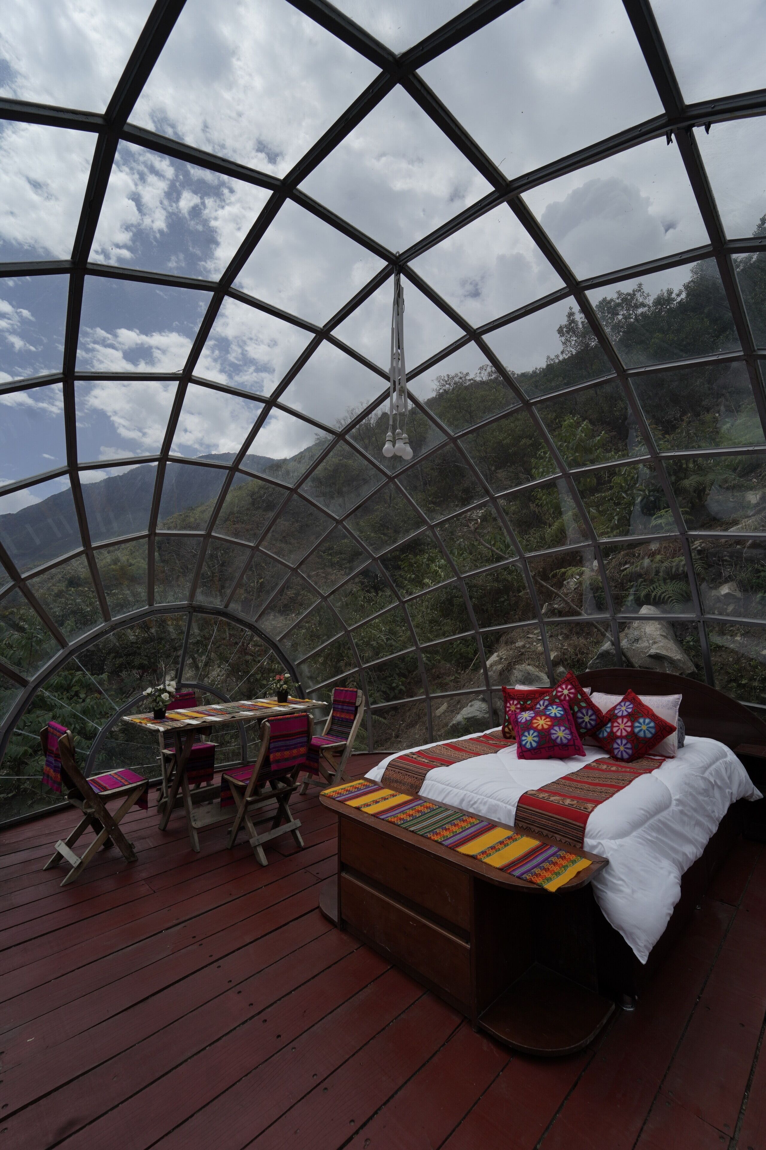 Una habitación en forma de cúpula con una cama, una mesa y sillas, rodeada por una terraza de madera.