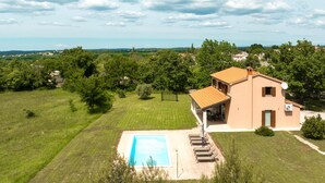 Una casa con piscina, rodeada de césped cuidado y árboles.