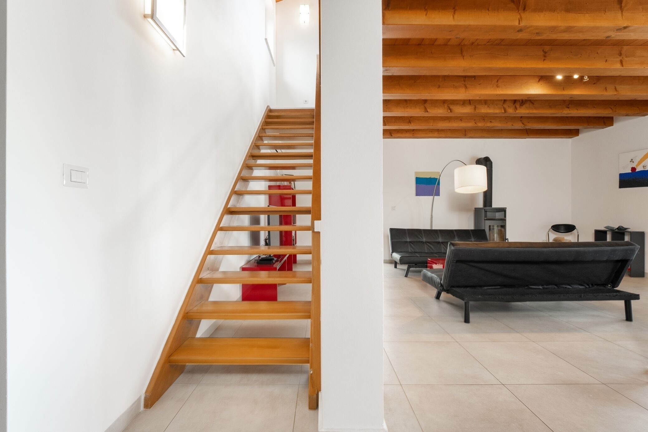 A staircase with wooden steps leading to a living area with a black sofa and a lamp.