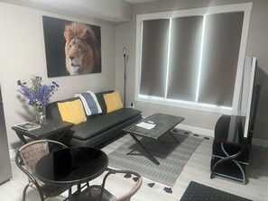 Una sala de estar con un sofá, una mesa de centro, una silla, un televisor y una ventana con persianas.
