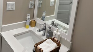 Une salle de bain avec un lavabo blanc, un miroir et un panier en bois contenant une serviette blanche.