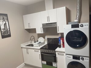 A compact kitchen with white cabinets, a dishwasher, a washing machine, and a stove. - Beautiful crib (Prince George)