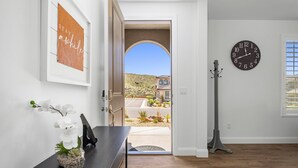 Ein Zimmer mit Holzboden, einem Schreibtisch mit einer Vase weißer Blumen, einem gerahmten Schild an der Wand, einer Uhr und Blick auf ein Gebäude durch eine offene Tür.