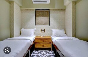 A small, clean room with two single beds, a wooden nightstand, and a wall-mounted air conditioning unit. - Tokyo Stay Hostel (Mumbai)