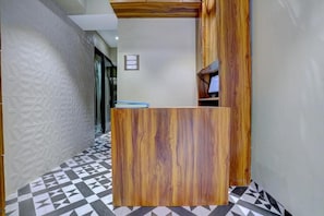A reception desk with a wooden finish, a geometric patterned floor, and a white textured wall. - Tokyo Stay Hostel (Mumbai)