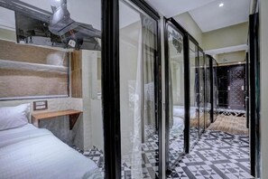 A modern hotel room with a large bed, a wooden shelf, and a glass partition. - Tokyo Stay Hostel (Mumbai)