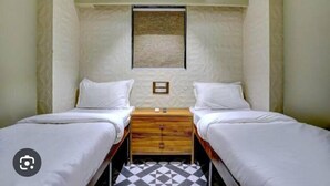 A small, clean room with two single beds, a wooden nightstand, and a wall-mounted air conditioning unit. - Tokyo Stay Hostel (Mumbai)
