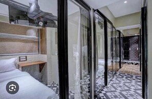 A hotel room with a bed, a bedside table, a large window, and a view of the outside. - Tokyo Stay Hostel (Mumbai)