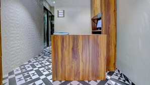 A reception desk with a wooden finish, a geometric patterned floor, and a white textured wall. - Tokyo Stay Hostel (Mumbai)