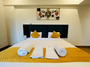 A hotel room with a bed, a headboard, a wall art piece, and towels on the bed. - Hotel Amahi Inn Sector 30 (Gurugram)