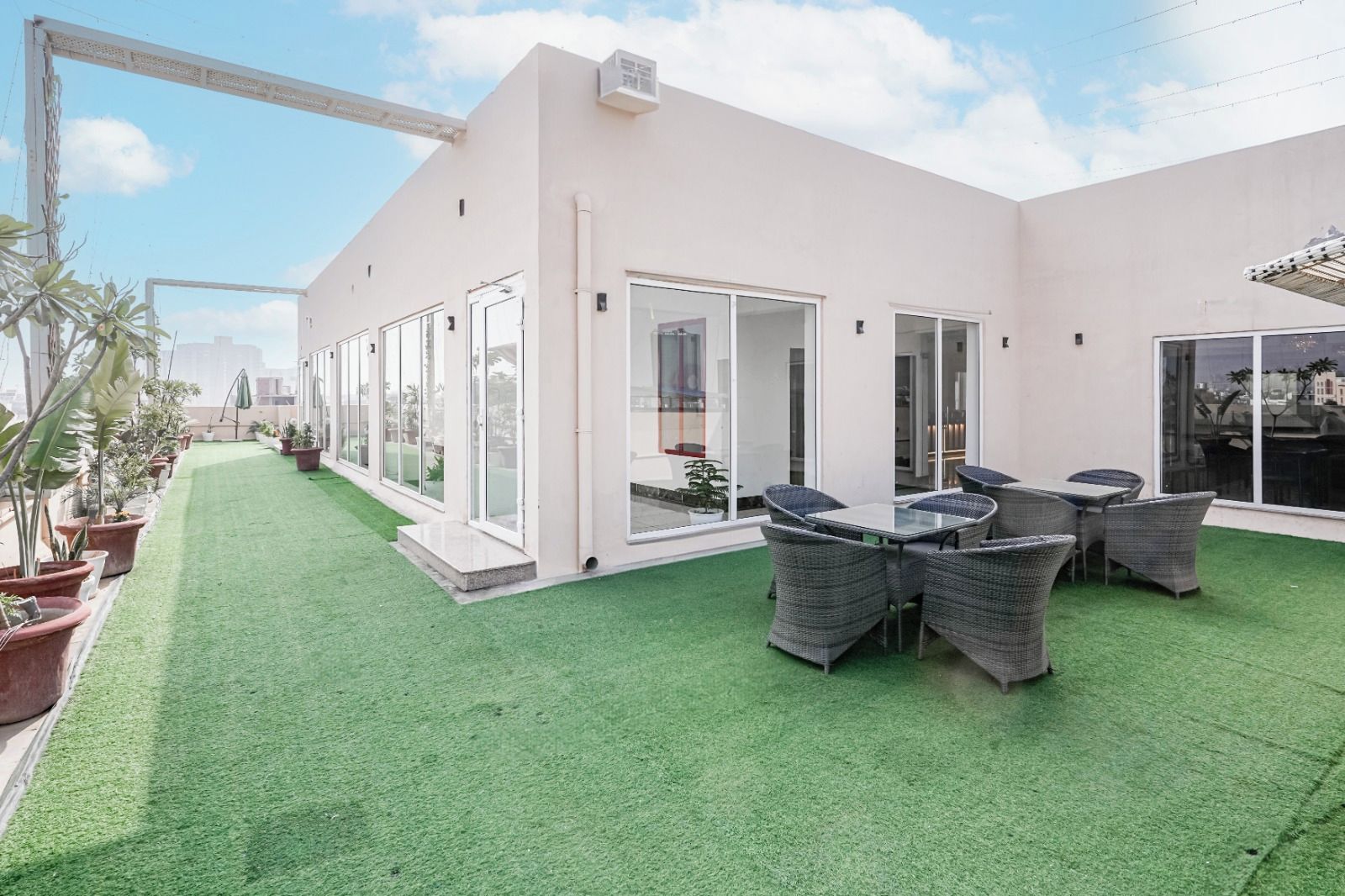 A modern building with a patio area featuring artificial grass, outdoor seating, and potted plants.