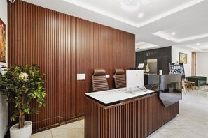 A modern reception desk with two leather chairs, a marble countertop, and a wooden panel wall. - Hotel Amahi Inn Sector 30 (Gurugram)