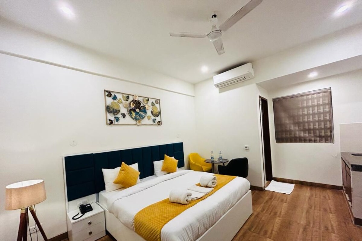 A hotel room with a bed, bedside table, lamp, ceiling fan, artwork, and a window.