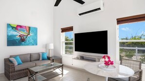 Ein modernes Wohnzimmer mit einer Couch, einem Couchtisch und Korbstühlen. Ein Flachbildfernseher ist an der Wand montiert und ein Gemälde hängt dort.
