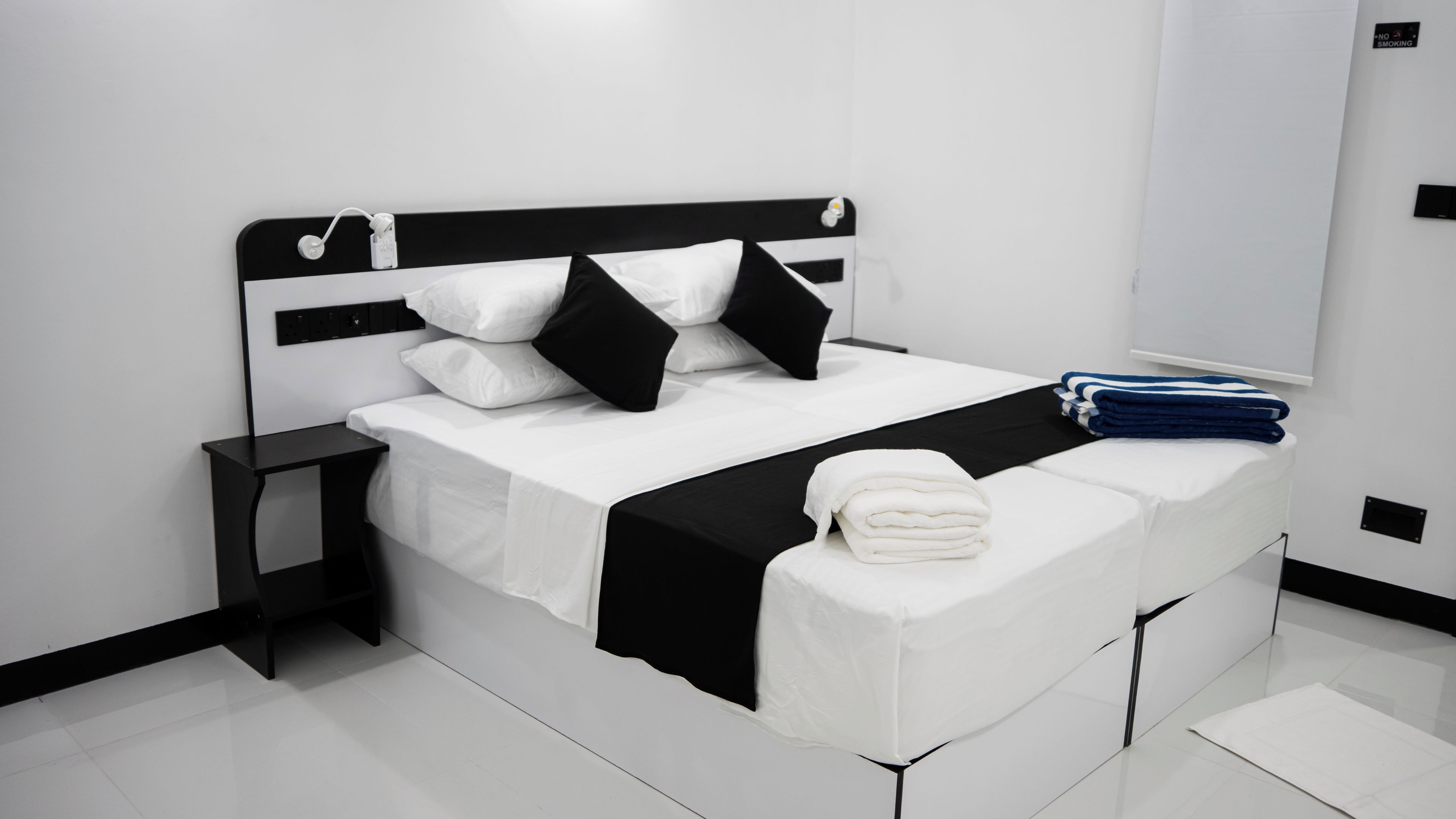 A modern hotel room with a black and white bed, a nightstand, and a neatly made bed with a folded towel.
