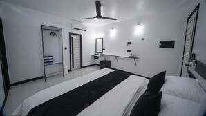 Et moderne hotelværelse med en stor seng, ventilator, garderobe, lille natbord med lampe og et spejl på væggen.