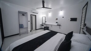 Una habitación de hotel moderna con una cama grande, un ventilador de techo, un armario, una mesita de noche pequeña con una lámpara y un espejo en la pared.