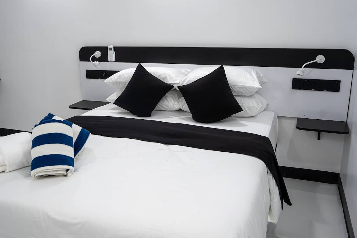 A neatly made bed with white and black bedding, a striped towel, and a black pillow. There are two bedside tables with a phone and a lamp on each.