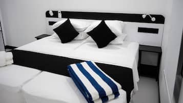 A neatly made bed with white and black bedding, a bedside table with a lamp, and a power outlet on the wall.
