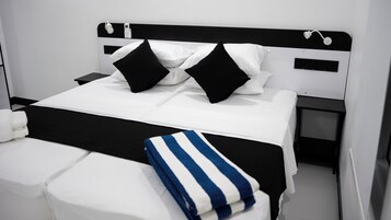 Una cama bien hecha con ropa de cama blanca y negra, una mesita de noche con una lámpara y un enchufe en la pared.