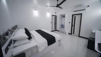 A modern hotel room with a bed, bedside table, ceiling fan, air conditioning unit, and a wardrobe.