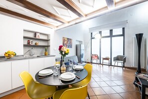 Eine moderne Küche mit Essbereich, mit einem runden Tisch und gelben Stühlen, einem eingebauten Backofen und einem großen Fenster mit Blick.