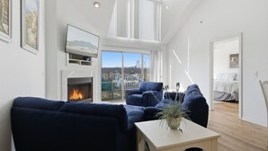 A modern living room with a fireplace, blue sofas, a white coffee table, and a balcony with a view. - Blue Oasis - Two Pools, Beach, & More! (Osage Beach)