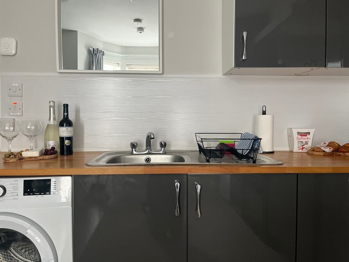 A modern kitchen with a stainless steel sink, a washing machine, and a wine bottle on the countertop.