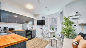 A compact kitchen with modern appliances, a dining area with a white table and chairs, and a cozy seating area with a sofa and a small side table. - Portrush Harbour Apt Walk to Beach (Portrush)