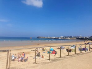 A beach with a clear sky, a sandy shore, and a distant cityscape.