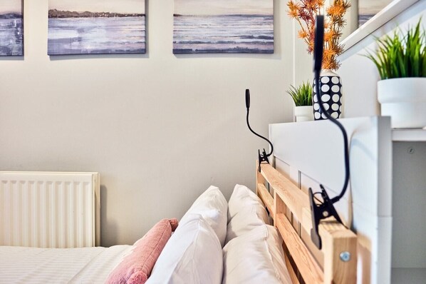 A bedroom with a wooden headboard, white bedding, a radiator, and wall-mounted artwork.