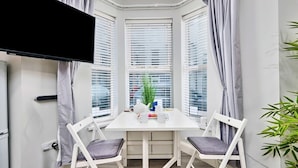 A corner room with a white table, two chairs, a TV, and a window with blinds. - Portrush Harbour Apt Walk to Beach (Portrush)
