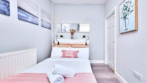 A bedroom with a bed, a bedside table, a mirror, and artwork on the walls. - Portrush Harbour Apt Walk to Beach (Portrush)