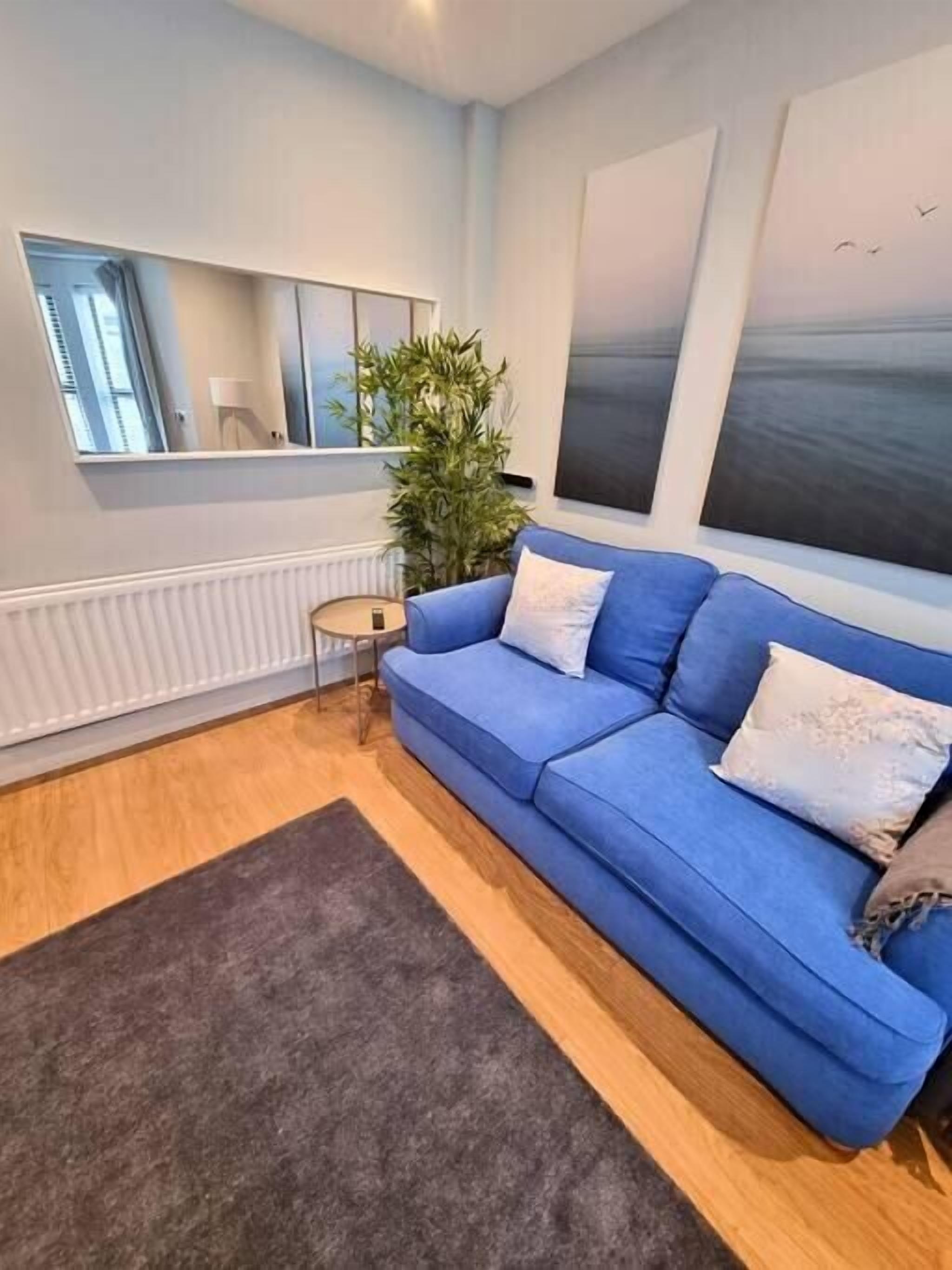 Un salon moderne avec un canapé bleu, un grand miroir, une plante en pot et des œuvres d’art accrochées aux murs.