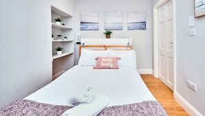 Une chambre bien rangée, avec un lit, des tables de chevet, une étagère avec des plantes et des œuvres d’art accrochées au mur.